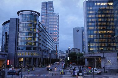 Brüksel, Brabant, Belçika 10: 12 2024 Günbatımında cam cepheli modern ofis binalarının yer aldığı bir şehir manzarası. Sokaklar yayalar ve araçlarla dolu ve gökyüzü bulutlu..