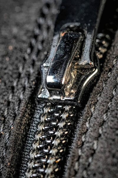 Крупный план металлической молнии на черной ткани, с детальным стежком и текстурой.