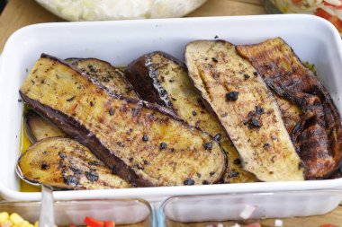 Lezzetli ızgara patlıcan dilimleri beyaz bir tabakta serpilmiş zeytinyağı ve üzerine karabiber serpiştirilmiş. Patlıcan, bazı kömürleşmiş kenarları ile altın-kahverengi bir renge sahiptir. Bu da dumanlı bir tadı gösterir..