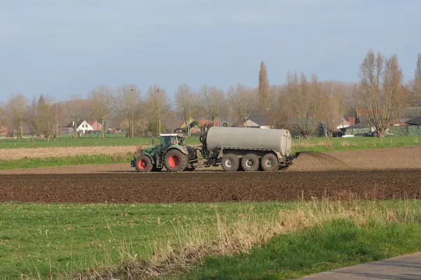 Bir tarım traktörü büyük bir tankı çekiyor ve tarım arazilerine gübre yayıyor. Tarla sürülüyor ve bu kırsal alanda ekilmeye hazır..