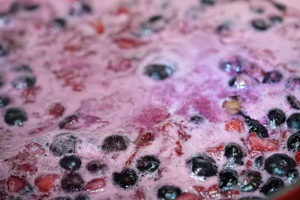 Görüntü yaban mersinleri ve doğranmış çileklerin yakın çekimini gösteriyor. Karışım köpürüyor ve güzel, canlı bir renk yaratıyor. Yemek fotoğrafçılığı.