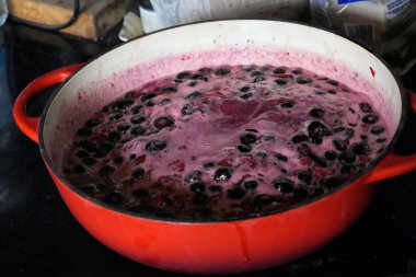 Koyu böğürtlen ve yakut kırmızısı meyvelerle dolu canlı kırmızı bir tencere. Ev yapımı reçel ya da komposto oluşturma sahnesi.