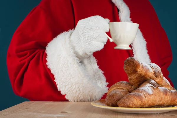 Noel Baba bir fincan kahve tutuyor ve gurme kruvasan yiyor. Size iyi Noeller ve yeni yıl havası dilerim. Evde ya da kafede sıcak içeceklerle rahat..
