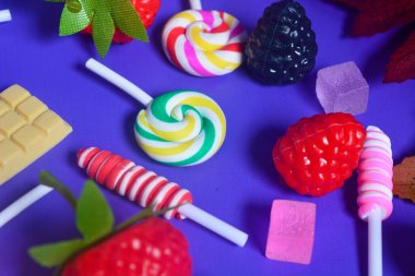 Tatlı atıştırmalıklar, şekerler, çikolatalar, mor arka planda lolipoplar.