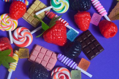 Tatlı atıştırmalıklar, şekerler, çikolatalar, mor arka planda lolipoplar.