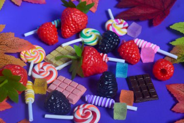 Tatlı atıştırmalıklar, şekerler, çikolatalar, mor arka planda lolipoplar.