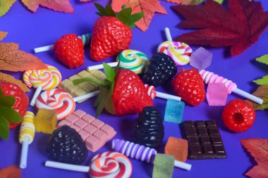 Tatlı atıştırmalıklar, şekerler, çikolatalar, mor arka planda lolipoplar.