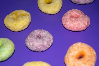 Pembe arka planda lezzetli görünen çeşitli renkte tatlı çörekler.