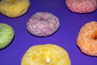 Pembe arka planda lezzetli görünen çeşitli renkte tatlı çörekler.