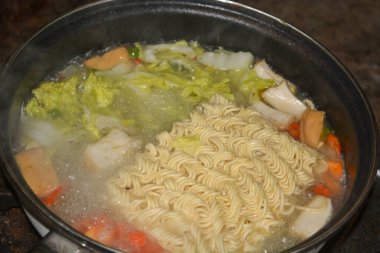 Photo of a pot of noodles being cooked with some vegetable toppings