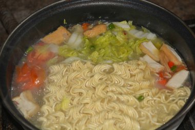 Photo of a pot of noodles being cooked with some vegetable toppings