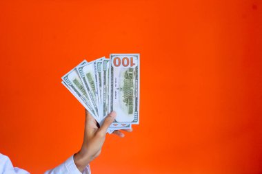 16 Ocak 2024, kredi ve kredi konseptleri. Elinde dolar olan gülümseyen Asyalı bir kadın ve kamera karşısında mutlu görünüyor, turuncu arka plan. Endonezya