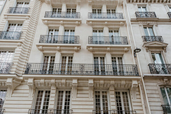 Exterior of aged residential building of beige color with glass windows and beautiful cast iron balconies located in the center of Paris, France