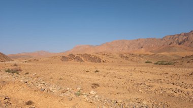 Ön planda kum ve kayalar olan çöl manzarası. 