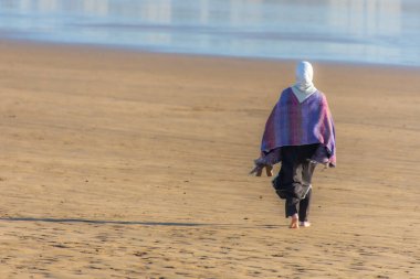 Essaouira, Fas: 29 Ekim 2024 - Fas 'ta plaj boyunca yürüyen Müslüman kadının arkadan görünüşü.