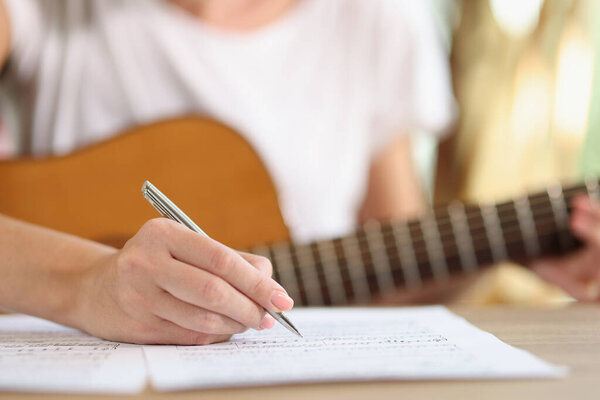 Close-up of female hand writing notes of new song. New ideas inspirational singer composing music with guitar at home. Music art concept