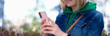 Smiling woman looks at phone on street. Getting good news in chat concept