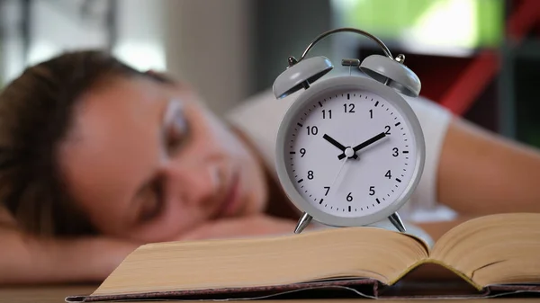 大书上灰色闹钟的特写和背景上睡觉的女人 教育时间 学习概念 — 图库照片