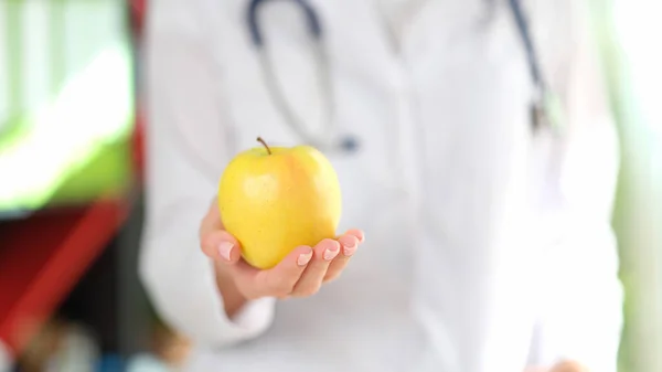 Close-up of doctor holding ripe yellow apple in hand. Healthy food, diet, vitamins and balanced nutrition concept