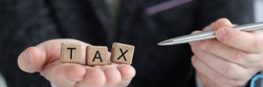 Tax text on wooden cubes and businessman with pen. Tax payments and credit concept