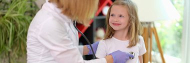 Doctor pediatrician listens with stethoscope to heartbeat of little girl in clinic. Medina child insurance concept