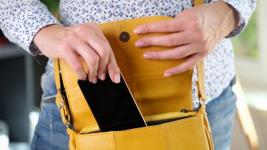 Kadın akıllı telefonunu sarı çantaya koyuyor. Cep telefonunu güvende tut ve seyahat ederken önemli bilgiler al.