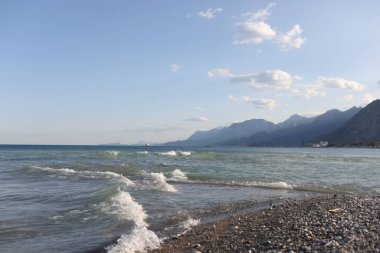 Sisli dağların arka planında mavi gökyüzü olan çakıl taşları plajına yakın çekim. Dağ manzarası. Resimli deniz kıyısı. Yaz zamanı, plaj tatili konsepti.