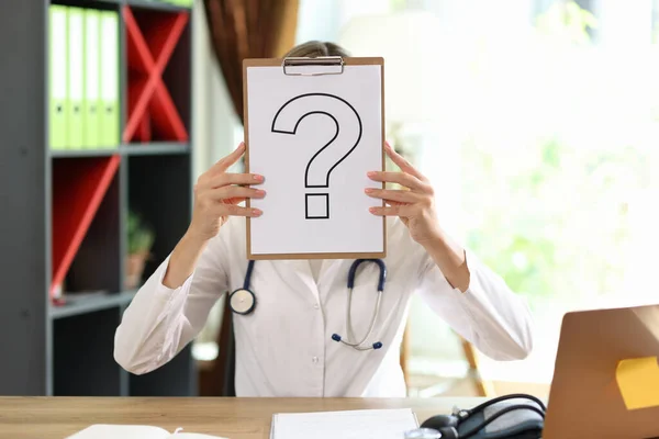 Stock image Close-up of woman practitioner covering face with paper with question mark. Medical issues concept