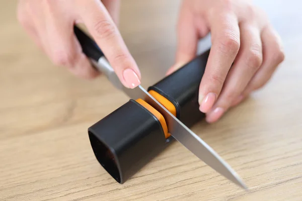 Close-up of female hands sharpening knife with special knife sharpener. Grindstone, kitchen tools and devices concept