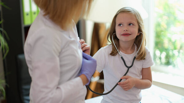 Портрет улыбающегося малыша, использующего медицинский стетоскоп на приеме у врача. Здравоохранение, медицина и детство