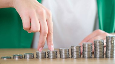 Kadın parmaklarının gümüş paraların toplandığı bar çizelgesine yakın plan çekimleri. İş büyümesi, gelir artışı, tekdüzelik ve başarı kavramı