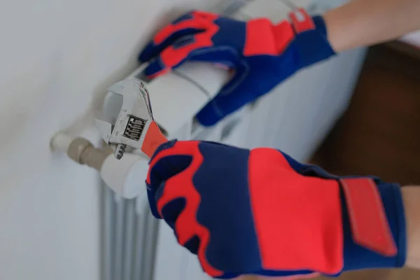 Close-up of man plumber hands in gloves installing heating radiator using wrench. Man builder installs new hot water central heating system using wrench