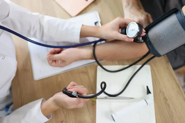 Stock image Female doctor using sphygmomanometer checks patients blood pressure in medical clinic. Top view of medical examination in hospital.