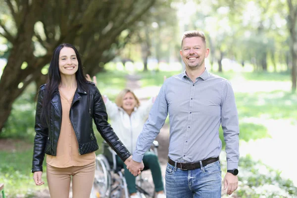 stock image Lack of attention to people with disabilities. Smiling couple walking in park and worried woman in wheelchair behind them.