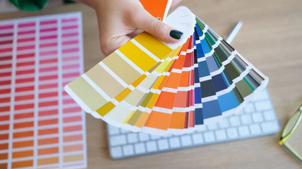 stock image Womans hand holds color swatches over her desk. Graphic designer chooses color from sampler for future project in studio.