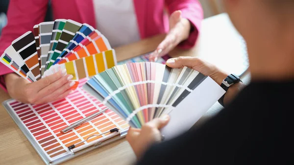 Manager helps client choose color from variety of samples in office. Close-up of color selection process in art studio.