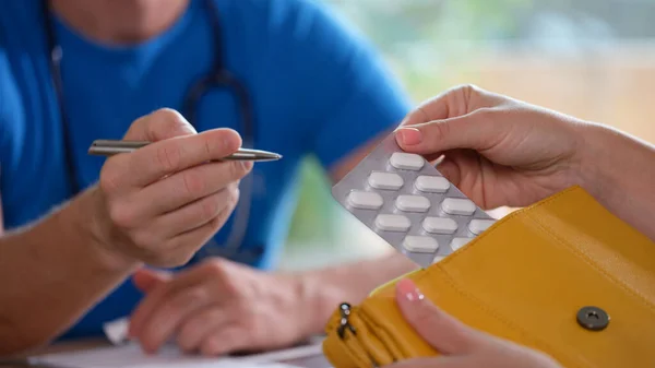 stock image Male doctor gives prescription for pills to woman in his clinic. Doctor and female patient sit at table and discuss medical drugs.