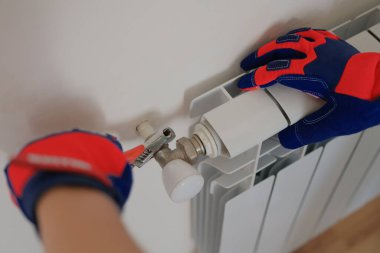 Eldiven ustası eve ısıtma pili takıyor. Tesisatçıların yakın çekimleri apartmandaki ısıtma bataryalarını tamir ediyor..