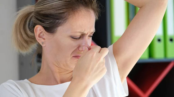 Unhappy woman smells her armpit close up. Unpleasant smell under armpit and health problem concept.