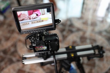 Digital camera with external monitor on camera slider filming woman typing on keyboard. Professional video production and cinema equipment.