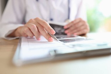 Close up of doctor is engaged in paper work, fills in medical records of patients. Female doctor analyzes ultrasound images of patients in her office.