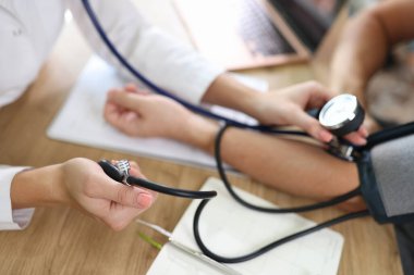 Close up of doctor using sphygmomanometer with stethoscope checks blood pressure of patient in hospital. Health care and medical examination concept.