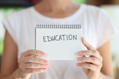 Woman holding notebook with word education on white page close up. Study, learning and school concept.