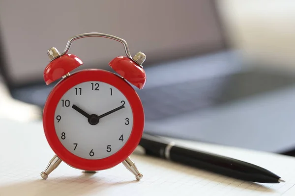 stock image Alarm clock with pen on blank page with blurry laptop in background. Time for creativity and writing goals for future concept.