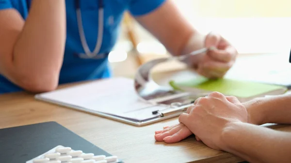 Doctor reading patients diagnosis and examining medical test results on his desk. Doctor and patient sitting at table in medical clinic close up.