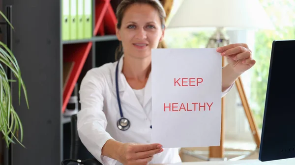Female doctor showing paper with words keep healthy at her medical office. Doctors recommendation and healthy lifestyle concept.