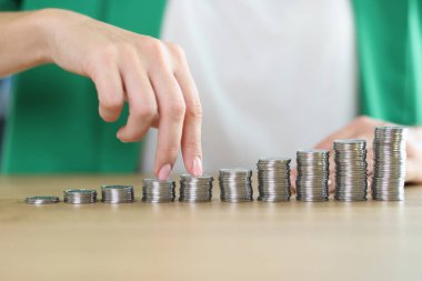 Womens fingers move over growing stacks of coins on table close-up. Investments, increasing income and developing business concept.