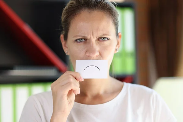 Frustrated woman covered her mouth with paper with sad emoticon. Sadness, disappointing and exhausting concept.