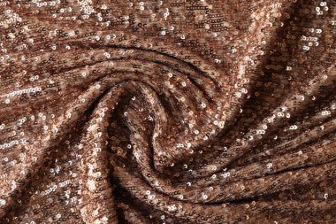 Brown textile decorated by plastic as background. Wavy fabric with shiny decoration close up.