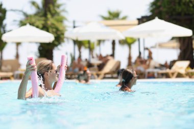 Women relax in resort pool on sunny day. Several hotel guests spend time in swimming pool with clear blue water.